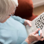 A woman works on a crossword puzzle, a type of brain game. | Corporate Synergies