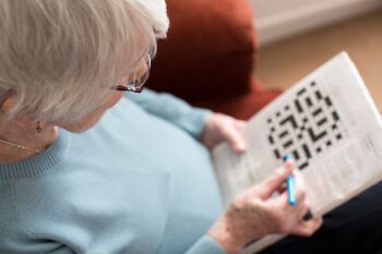 A woman works on a crossword puzzle, a type of brain game. | Corporate Synergies