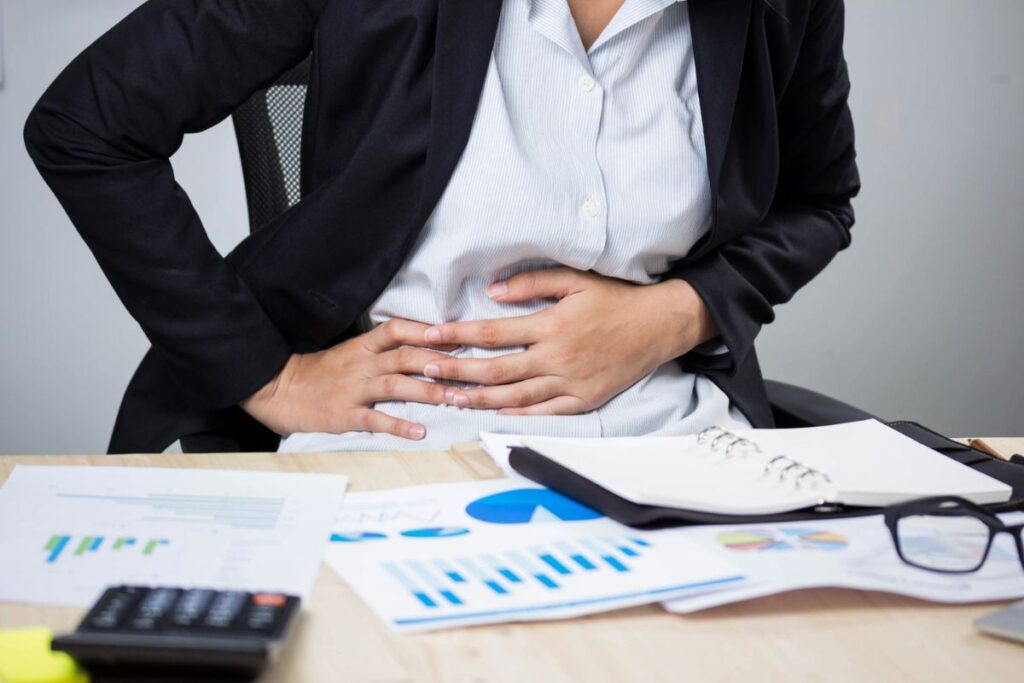 Businessperson at desk holding stomach in pain | Corporate Synergies