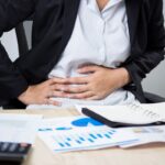 Businessperson at desk holding stomach in pain | Corporate Synergies