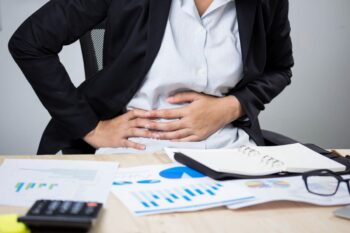 Businessperson at desk holding stomach in pain | Corporate Synergies