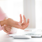 Woman holding her wrist in pain from using computer when not practicing ergonomics | Corporate Synergies