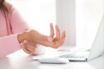 Woman holding her wrist in pain from using computer when not practicing ergonomics | Corporate Synergies