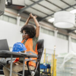 Multiracial female stretches at warehouse desk to benefit from ergonomics in the workplace | Corporate Synergies