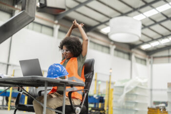 Multiracial female stretches at warehouse desk to benefit from ergonomics in the workplace | Corporate Synergies