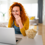 young woman using laptop while eating popcorn for good nutrition for remote work | Corporate Synergies