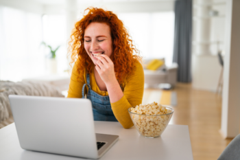 young woman using laptop while eating popcorn for good nutrition for remote work | Corporate Synergies
