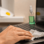 Male hand disinfects laptop keyboard with alcohol wipe to combat common workplace illnesses | Corporate Synergies