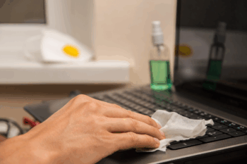 Male hand disinfects laptop keyboard with alcohol wipe to combat common workplace illnesses | Corporate Synergies