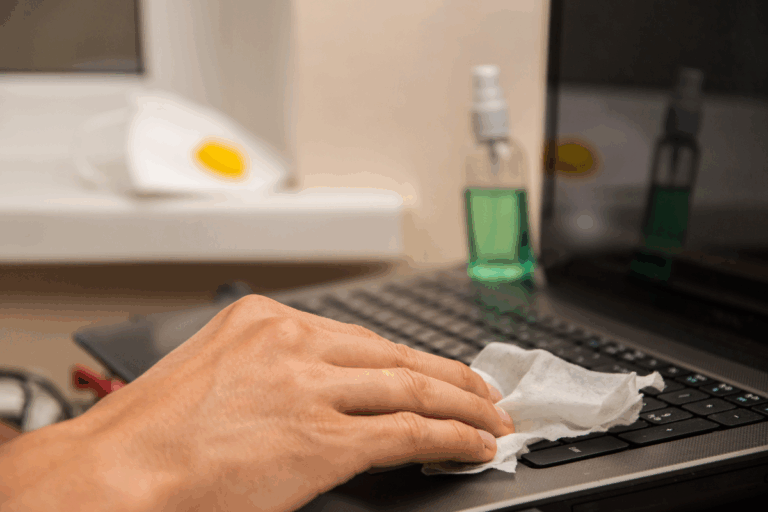 Male hand disinfects laptop keyboard with alcohol wipe to combat common workplace illnesses | Corporate Synergies