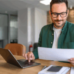 Man confidently reviewing household budget practicing financial wellness at his home computer | Corporate Synergies