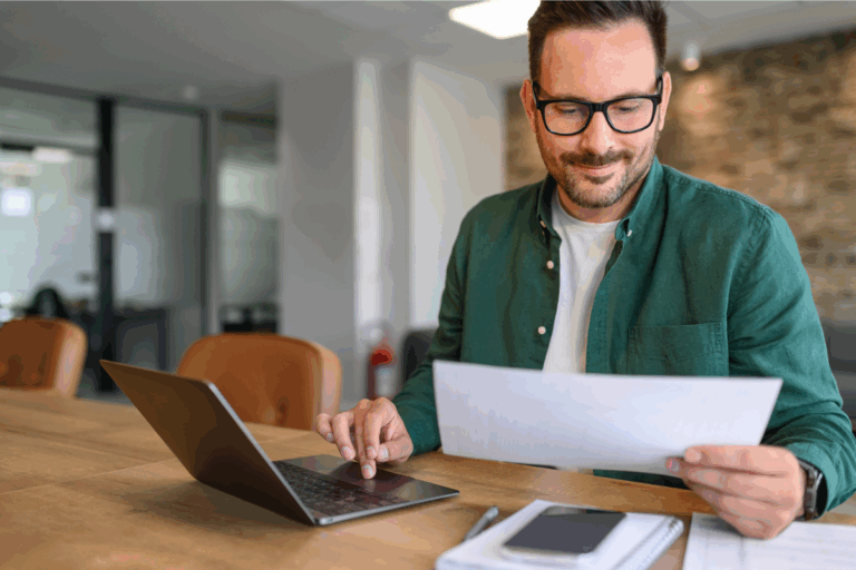 Man confidently reviewing household budget practicing financial wellness at his home computer | Corporate Synergies