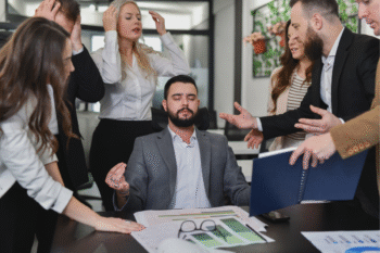 Frustrated employees with high-stress jobs behind manager who is meditating for mental resilience | Corporate Synergies
