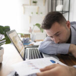 Depressed male worker at laptop thinking of ways to prevent burnout in the workplace | Corporate Synergies