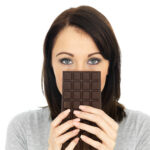 Young woman holding dark chocolate bar over her face for stress support | Corporate Synergies