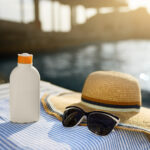 Sunscreen, sunglasses and hat on beach towel for heat safety | Corporate Synergies