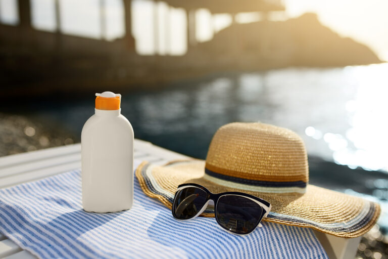 Sunscreen, sunglasses and hat on beach towel for heat safety | Corporate Synergies